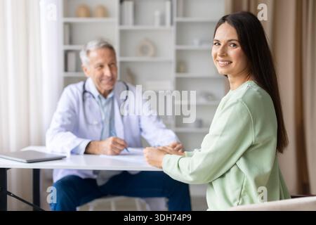 Lächelnde Patientin während eines Arzttermins mit einem Oberarzt im Hintergrund Stockfoto