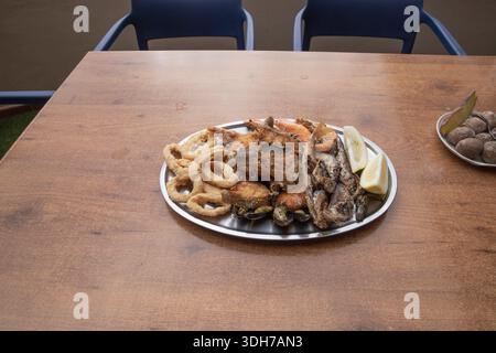 Gemischter frittierter Meeresfrüchte-Teller mit Garnelen, Calamari und Zitrone auf Holztisch Stockfoto