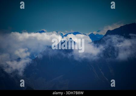 Dramatische, hochgelegene Berglandschaft mit zerklüfteten Gipfeln, die durch eine dicke Schicht weißer Wolken durchdringen. Die imposanten Berge von Titlis dominieren Stockfoto
