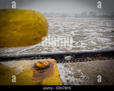 Schwimmendes Eis auf der gefrorenen Elbe durch ein gelbes Metallgeländer in Hamburg, Deutschland, an einem kalten Wintertag als Symbol für eiskalte Temperaturen Stockfoto