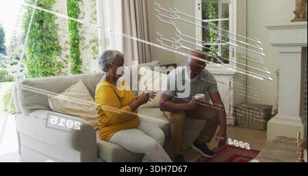 Ein Paar schlürft mit grauem Polo und Senftop und hält weiße Tassen im Wohnzimmer an Glastüren Stockfoto