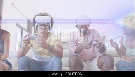 Zwei Erwachsene spielen, die weiße VR-Headsets tragen, lachen auf dem Wohnzimmer-Sofa und halten Gamecontroller Stockfoto