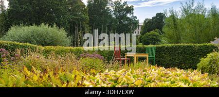 Eine ruhige schwedische Gartenszene des Herrenhauses Karlslund in Orebro mit lebendigen Blumenbeeten, üppigen Hecken und rustikalen Sitzgelegenheiten in Rot, Gelb und Grün Stockfoto