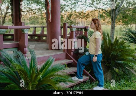 Junge rothaarige Frau, die Treppen zu einer Gartenlaube im Freien in einem öffentlichen Park hinaufgeht. Stockfoto