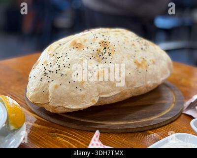 Frisch gebackener Brotlaib mit schwarzen Sesamsamen, auf Holzbrett im Innenbereich platziert. Mobiles Foto Stockfoto