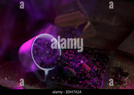 Kaffeebohnen aus einem Becher, ein Weihrauchkegel, der purpurnen Rauch ausstrahlt Stockfoto