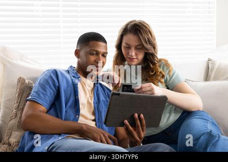 Verschiedene Paare sitzen auf Sofa in hellem Wohnzimmer, mit Tablet Folio Hülle und Kreditkarte Stockfoto