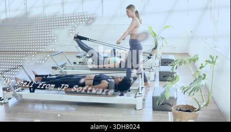 Leitender Trainer mit grauen Leggings, der zwei Frauen mit Reformern im Pilates-Studio führt Stockfoto