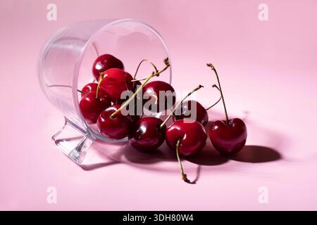 Glasbehälter auf rosa Hintergrund mit Kirschen Stockfoto