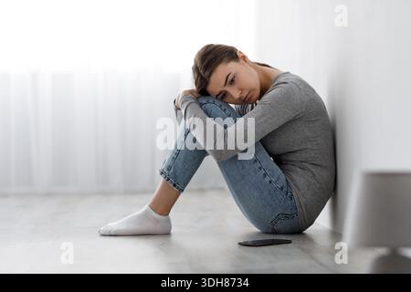 Gelangweilt verärgert depressive Dame auf dem Boden mit Smartphone sitzen, gleichgültig zu Seite Probleme haben Stockfoto