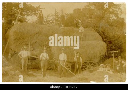 Postkarte aus der Edwardianischen Ära einer Gruppe von Männern zur Erntezeit, die Rechen halten, einen Pferdewagen mit Heu auf einen heurick entladen. Kinder sitzen im Vordergrund. Fotografie von Phillips, East Stour, Dorset, Großbritannien um 1910. Stockfoto