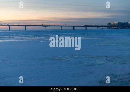 Panoramablick auf die Western High-Speed Diameter Brücke, die sich über den gefrorenen Golf von Finnland im Winter bei Dämmerung mit goldenem Sonnenuntergang erstreckt Stockfoto