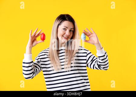 Osterfeier. Porträt einer lächelnden Frau, die bemalte Eier auf gelbem Hintergrund hält Stockfoto