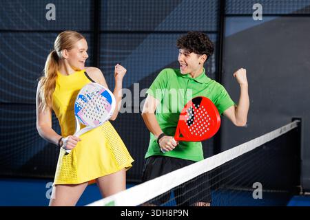 Glückliche Mann und Frau feiern den Siegerpunkt mit Padel-Schlägern auf dem Hallenplatz während des Spieltrainings und Turnierwettbewerbs Stockfoto