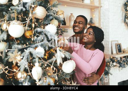 Ein Paar dekoriert Weihnachtsbaum mit Ornamenten und Lichtern in gemütlicher Innenumgebung in der Nähe der Feiertage Stockfoto