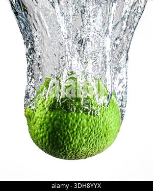 Ein Kalk wird in zwei Hälften geschnitten und in ein Glas Wasser geworfen. Der Kalk ist grün und das Wasser ist klar Stockfoto