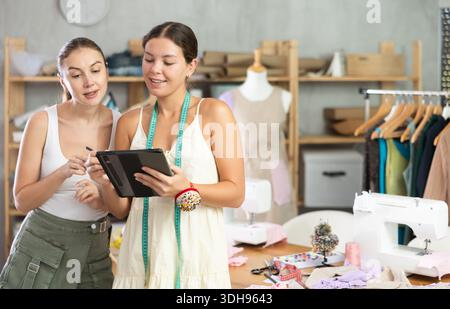 Zwei Schneiderinnen zeichnen ein Modell von Kleidung auf einem Tablet Stockfoto