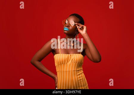 Glamouröse afroamerikanische Dame im hellen Outfit posiert auf Rot Stockfoto