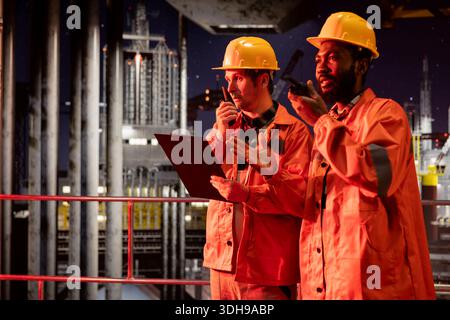 Diverse Ingenieurteams verwalten die Öl- und Brennstoffförderung über Walkie-Talkie-Funkgeräte auf Offshore-Plattformen und sorgen so für die Erdölkontrolle und das Management der Erdgasproduktion für die Kraftstoffindustrie. Stockfoto