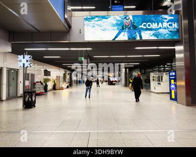 Krakau, Polen - 12. Januar 2026: Offener Krakauer Flughafenterminal mit Reisenden, Schildern und einem großen Overhead-Banner in einer hellen, modernen Halle. Stockfoto