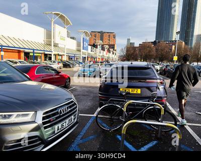 Manchester, Großbritannien - 14. Januar 2026: Belebter Parkplatz vor einem Einkaufszentrum mit Lamborghini SUV und Fahrrädern in der Nähe des Eingangs. Stockfoto