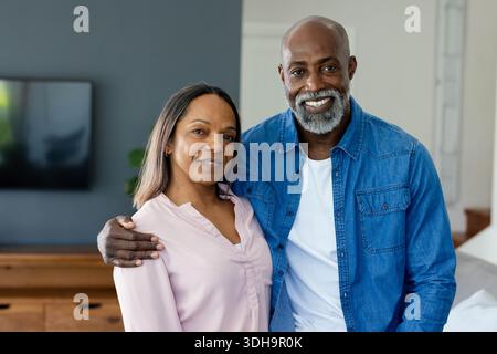 Älteres Paar steht im Wohnzimmer am Wandfernseher, Mann trägt Denim-Hemd, Frau trägt Bluse Stockfoto