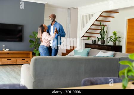 Verschiedene Paare tanzen und umarmen im Wohnzimmer mit grauem Sofa, Fernseher, Holzkonsole Stockfoto
