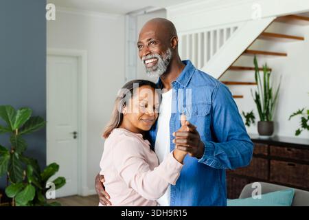 Ein reifes Paar tanzt in der Nähe der Treppe im Wohnzimmer, trägt ein Denim-Hemd und eine blassrosa Bluse Stockfoto