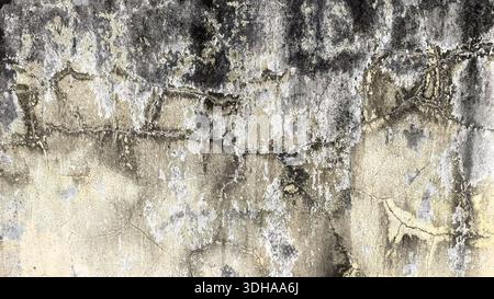 Eine Nahaufnahme einer stark verwitterten Wand mit sichtbaren Rissen, abblätternder beiger Farbe und dunklen Schimmelflecken, die eine griffige, veraltete Industrietextur erzeugen Stockfoto