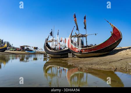 Traditionelles Mondboot (Sampan) an der Küste von Teknaf, Cox's Bazar. Buntes Holzfischboot an einem Sandstrand unter klarem blauen Himmel Stockfoto