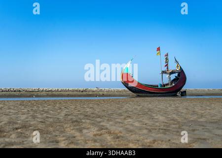 Traditionelles Mondboot (Sampan) an der Küste von Teknaf, Cox's Bazar. Buntes Holzfischboot an einem Sandstrand unter klarem blauen Himmel Stockfoto