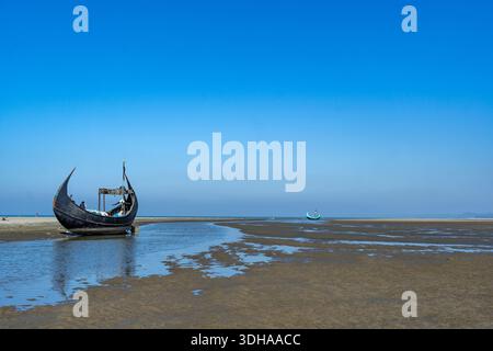 Traditionelles Mondboot (Sampan) an der Küste von Teknaf, Cox's Bazar. Buntes Holzfischboot an einem Sandstrand unter klarem blauen Himmel Stockfoto