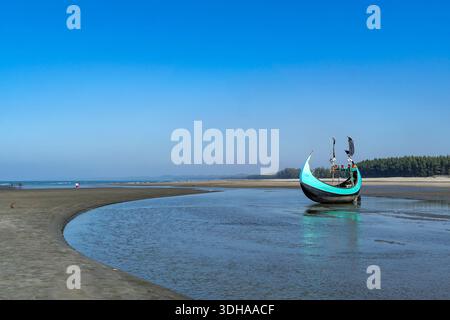 Traditionelles Mondboot (Sampan) an der Küste von Teknaf, Cox's Bazar. Buntes Holzfischboot an einem Sandstrand unter klarem blauen Himmel Stockfoto