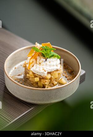 Ein raffiniertes Dessert mit einer Basis aus karamellisierten Äpfeln, garniert mit einem Schuss frischer Schlagsahne, Zitrusschale und Minzblatt. Stockfoto