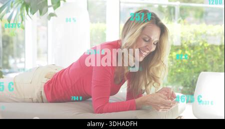 Liegende Frau in rosa Oberteil, lächelnd, Smartphone auf Sofa zu Hause an Fenstern, blaugrüne Überzüge Stockfoto