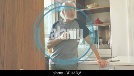 Stehender Mann in Raglanhemd, lehnt sich auf die Theke in der Küche, hält Becher, blauer Ring-Überzug sichtbar Stockfoto