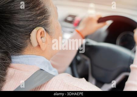 Ältere Frau mit Hörgerät hinter dem Lenkrad. Sicheres Fahren für ältere Menschen. Selektiver Fokus. Lebensstil-Konzept im Ruhestand. Stockfoto