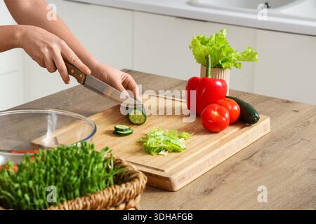 Weibliche Hände schneiden Gurke auf dem Tisch in der Küche Stockfoto