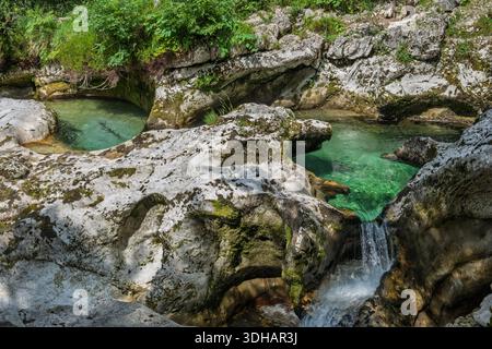 Klare türkisfarbene Pools und skulpturierte Kalksteinfelsen in der Mostnica-Schlucht, Slowenien, mit einem kleinen Wasserfall, der durch eine unberührte alpine Landschaft fließt. Stockfoto