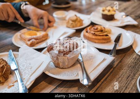 Verschiedene Gebäcksorten, Muffins, Zimtrollen, Scone und Gebäck auf Holztisch, Teller mit Besteck in der Bäckerei Stockfoto