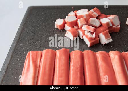 Die Krabbe klebt in Würfel geschnittene Surimi und klebt auf der Oberfläche des dunklen Schneidebretts Stockfoto