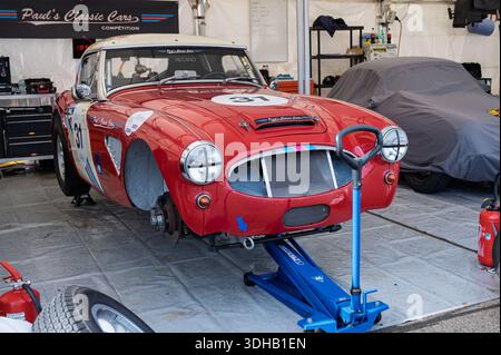 Ein klassischer roter Austin-Healey 3000 Mk II Rennwagen aus dem Jahr 1962, der mit Rennstreifen und der Nummer 31 verziert ist, wird auf einem Wagenheber ohne die Vorderräder angehoben Stockfoto