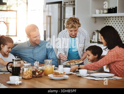 Fröhliche Familie, Pfannkuchen und Frühstück mit Großmutter für einen Snack am Morgen oder für eine gemeinsame Verbindung zu Hause. Mom, Dad und Opa, die mit Kindern essen, Kinder Stockfoto