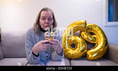 Frau feiert ihren 69. Geburtstag zu Hause mit goldenen Ballons und Kerzen Stockfoto