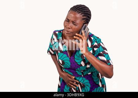 Schöne afrikanische Frau in kurvigem Lendenkleider über weißem Hintergrund, die Magenschmerzen spürt, während sie auf dem Handy spricht. Stockfoto