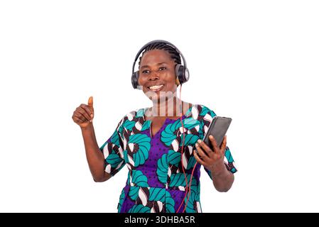 afrikanische Frau, die auf weißem Hintergrund steht, hört Musik mit Handy und Ohrhörern lachend. Stockfoto