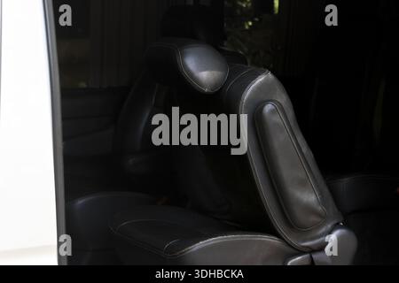 Bequemer Autositz aus schwarzem Leder im modernen Innenraum des Transporters mit schlankem Design, umklappbarer Armlehne und verstellbarer Kopfstütze für luxuriöse Reisen Stockfoto