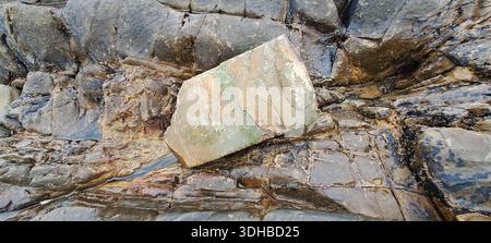 Wasser fließt nach Regen über dunkle Felsen an der Küste, mit einem flachen Stein auf der Spitze Stockfoto
