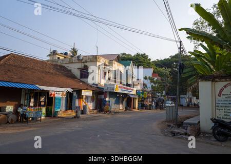Fort Kochi, Indien - 16. März 2023: Eine Straße in Fort Kochi bietet kleine Geschäfte mit Schildern auf Englisch und Malayalam, Fliesendächer, Überkopfkabel, ein paar Leute sitzen und gehen, eine Bananenfabrik und eine Wand mit institutionellen Informationen. Stockfoto