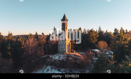 Der Aussichtsturm Stepanka steht hoch im Isergebirge, umgeben von schneebedeckten Bäumen. Der Sonnenuntergang wirft warmes Licht auf den Turm und schafft eine wunderschöne Szene. Stockfoto